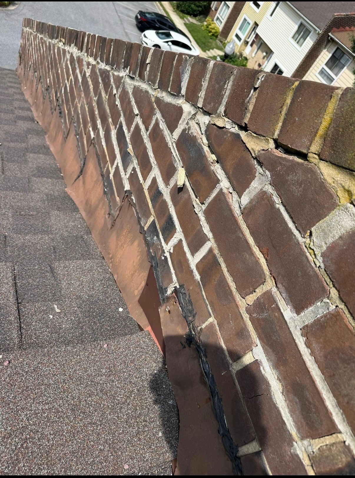 Close-up of a sloped rooftop brick parapet with white mortar and a view of houses below