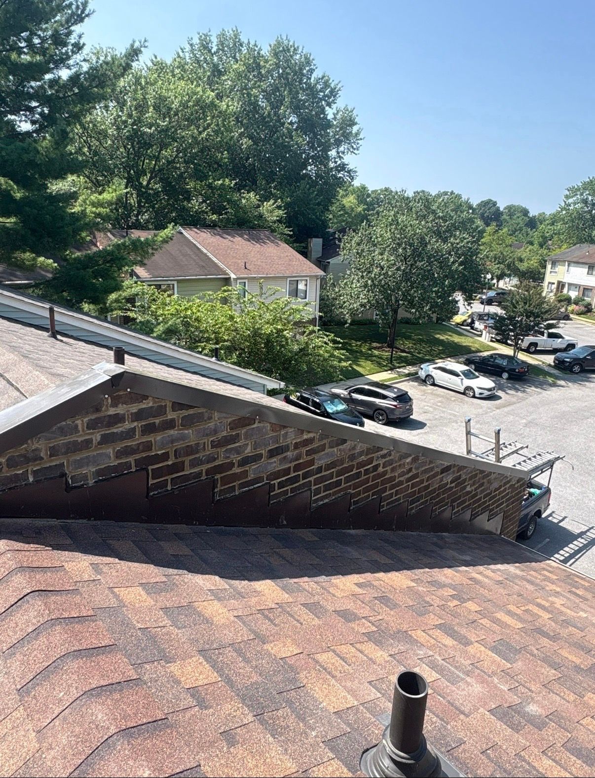View from a rooftop over a parking lot, trees, and nearby buildings on a sunny day
