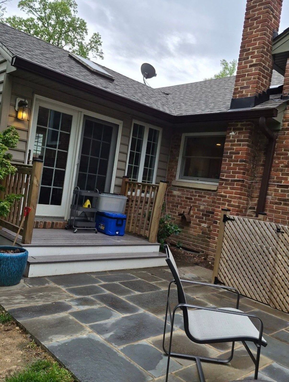 Brick patio with stone pavers, outdoor chair, and house patio doors beneath a covered roofline.