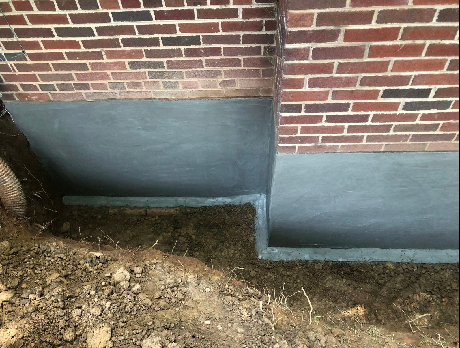 Brick house foundation with gray waterproofing and exposed dirt along the base outside.