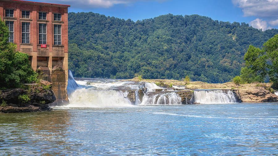 River and waterfall beside a red brick building with forested hills in the background