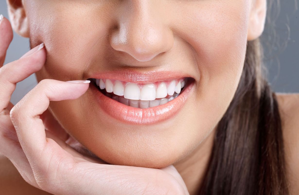 Close-up of a smiling mouth with white teeth, a finger touching the lower lip.