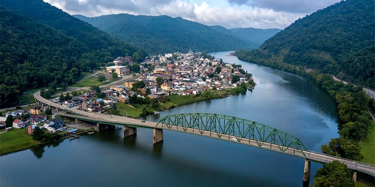 Aerial view of a riverside town beside a bridge, surrounded by green mountains and blue water