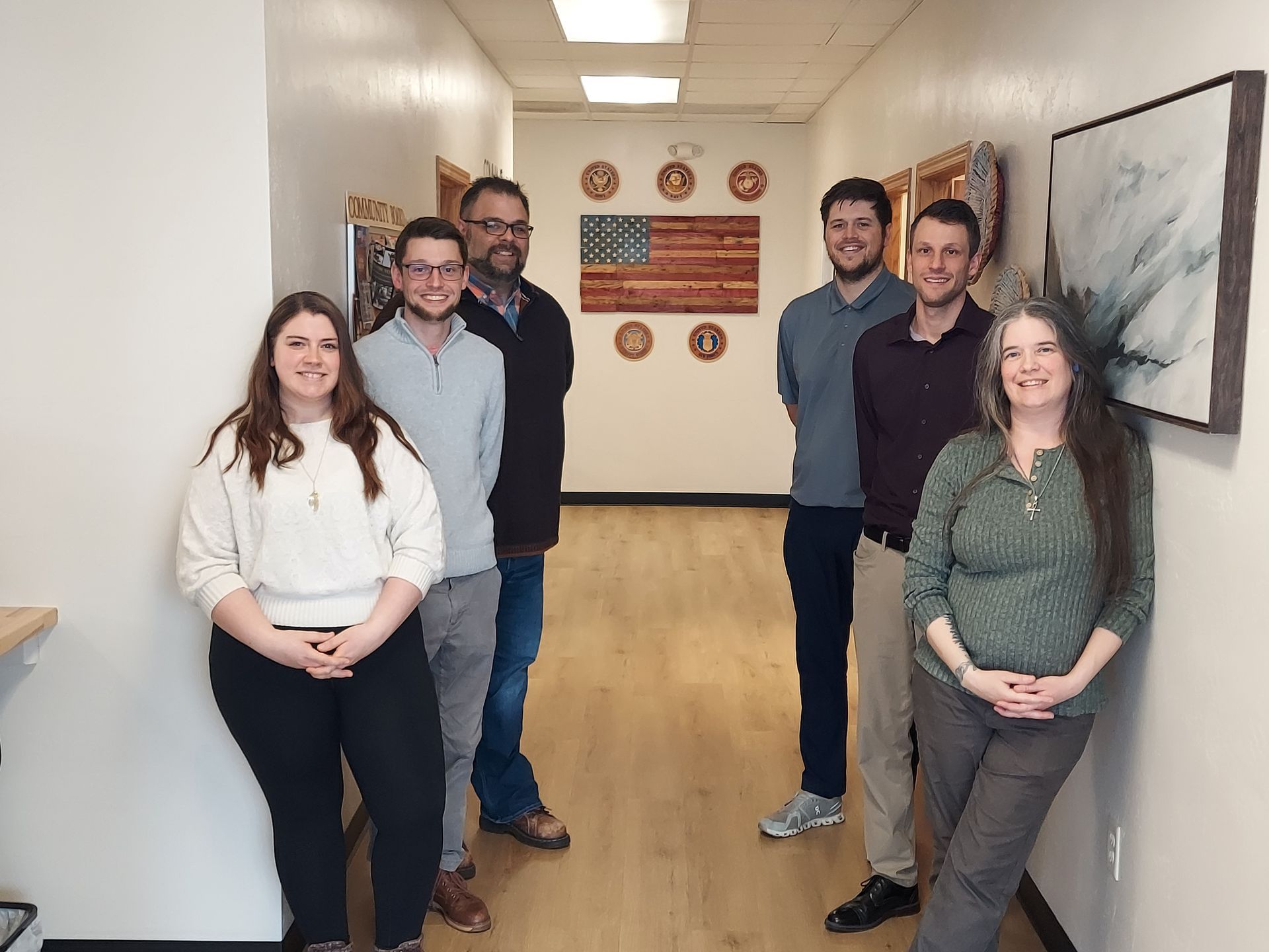 Six people are standing in a hallway, with framed art and wall clocks in the background.