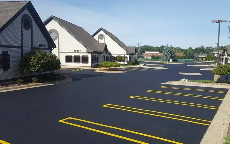 Paved parking lot with yellow painted parking spaces in front of a white building on a sunny day.