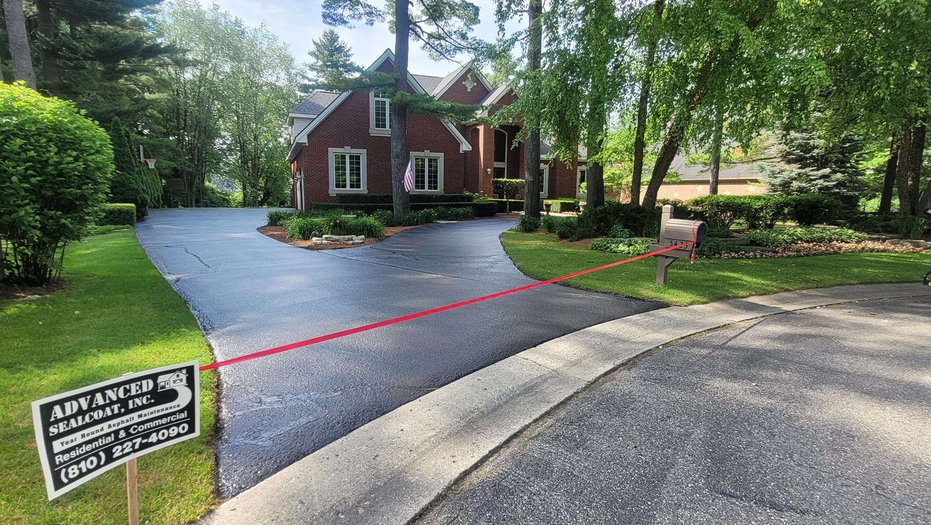 A house with a brick exterior and a curved driveway. A red line spans across the driveway, and a sign is present.