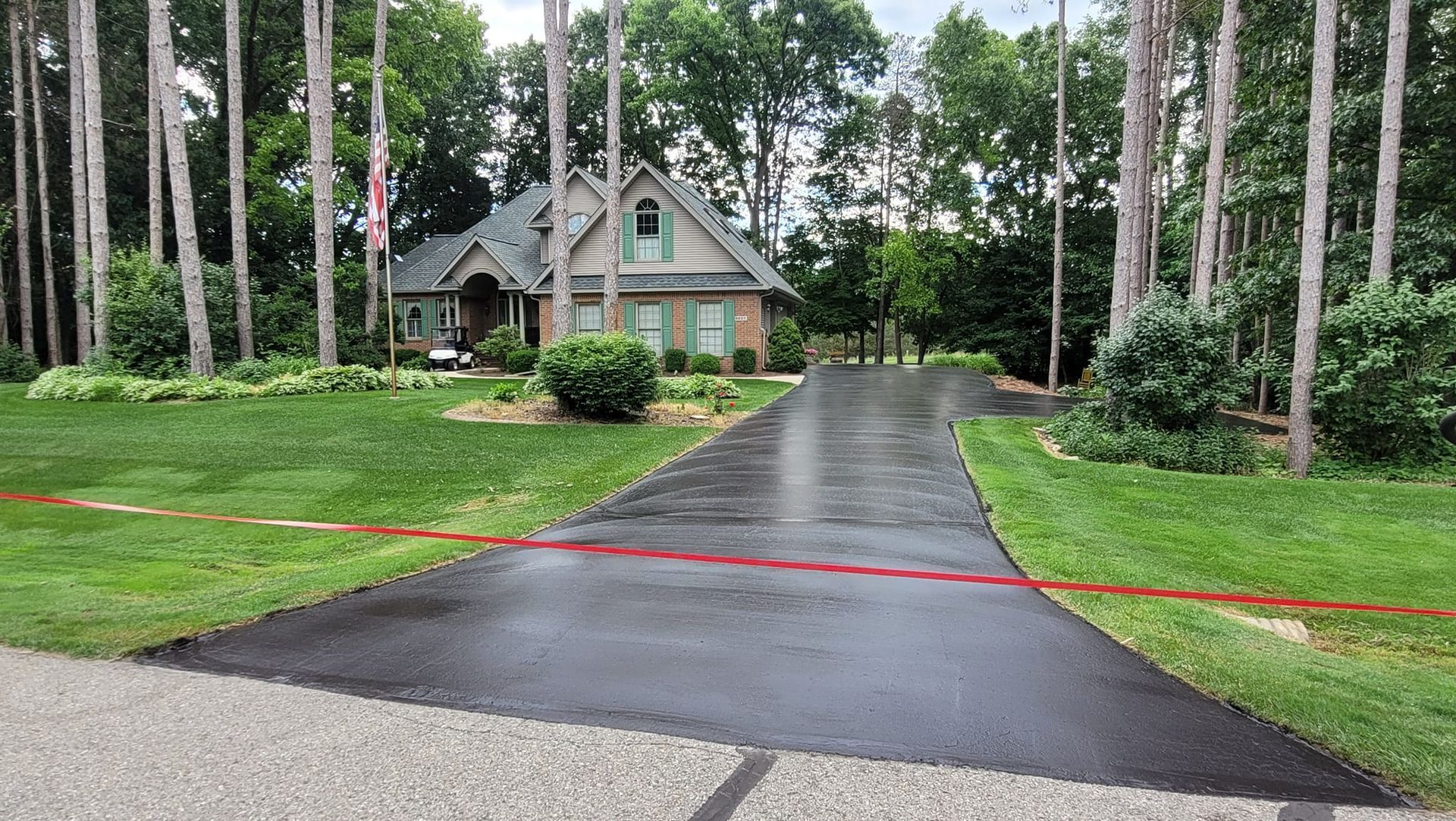 A house with a long, wet driveway surrounded by trees and grass.