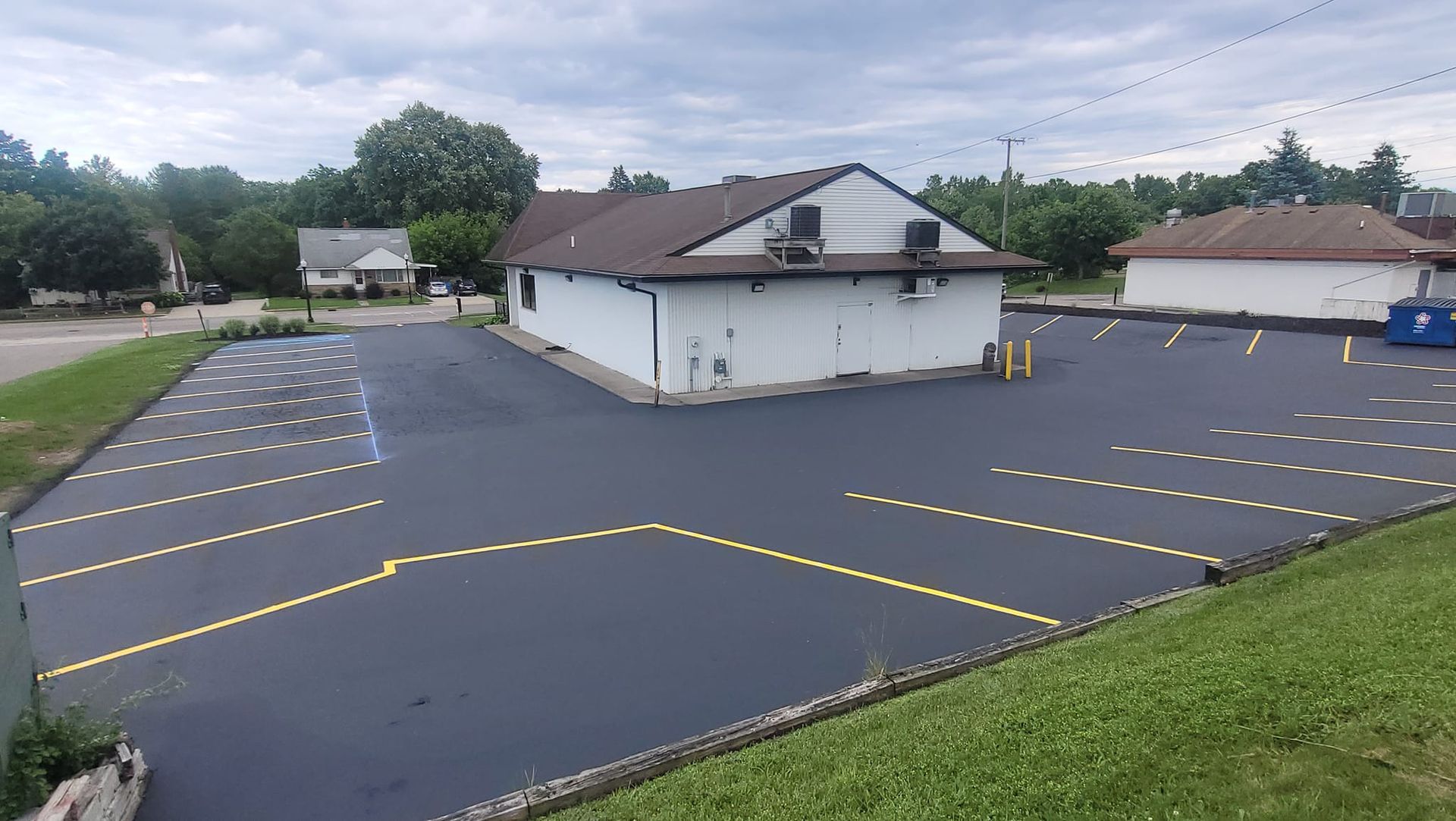 Newly paved parking lot with yellow parking lines and a white building in the center. Overcast day.