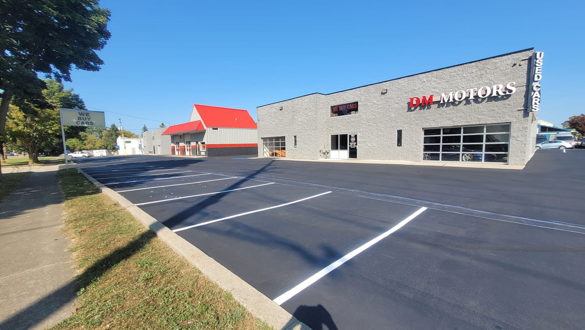 Exterior of J&M Motors auto dealership with a red roof and a black parking lot on a sunny day.