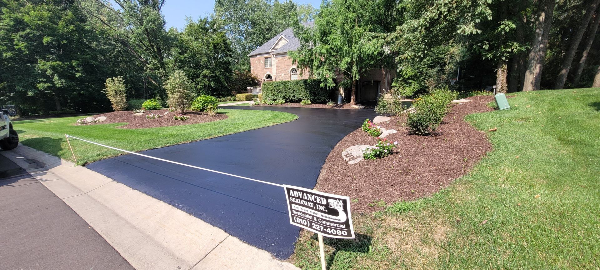 Newly sealed asphalt driveway leading to a house, with a yard edged with mulch and landscaping.