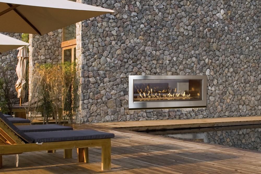 Fireplace built into a rock wall, beside a pool with lounge chairs and umbrellas.