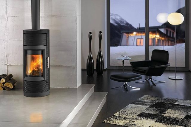 Modern living room with a lit fireplace, armchair, and window overlooking a snowy landscape.