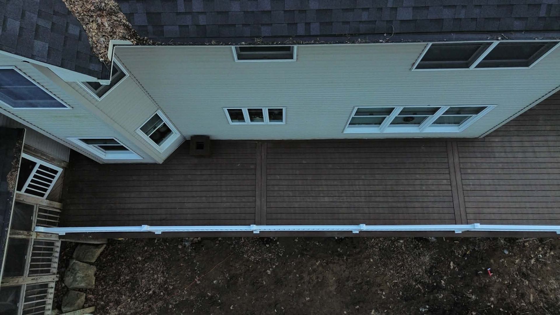 An aerial view of a tan two-story house with a large brown composite deck and white railings, overlooking a backyard.