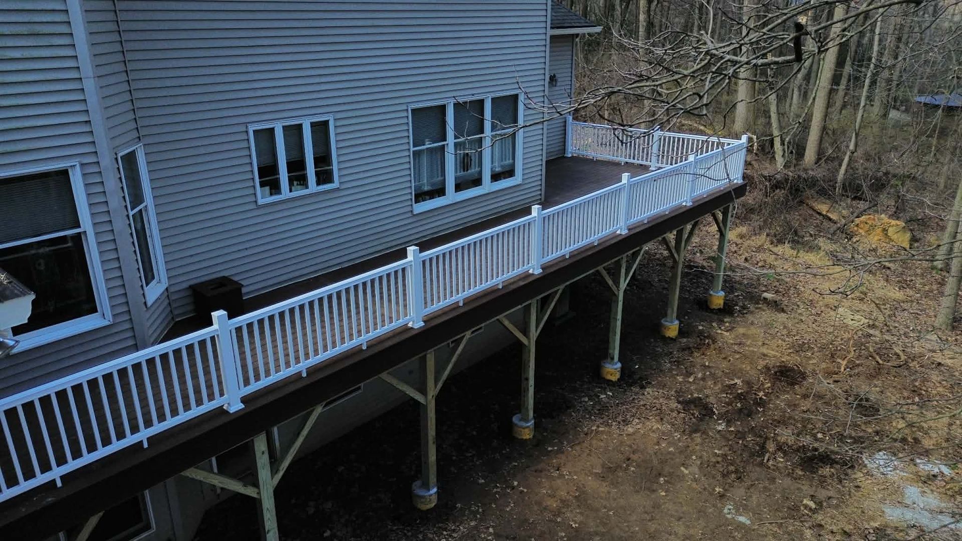 A high-angle view of a gray house exterior featuring a large, dark wood deck with white railings, set above a yard.