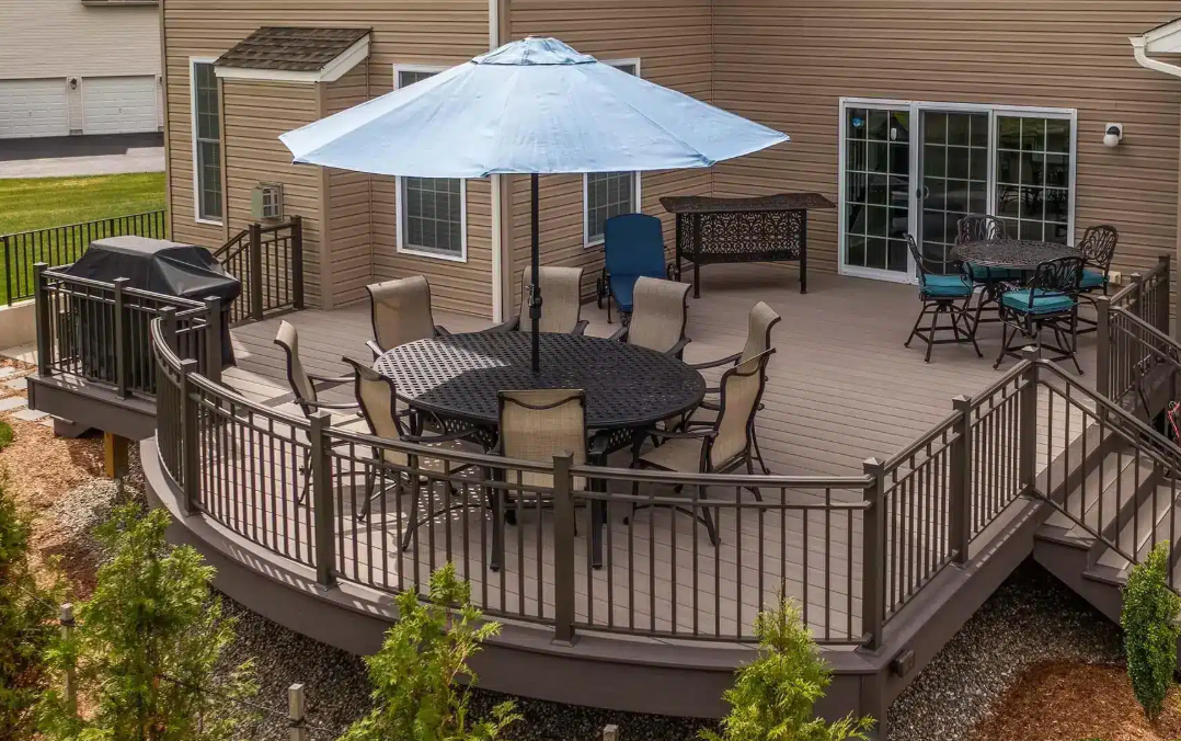 A multi-level outdoor deck with furniture, umbrella, and grill, next to a house