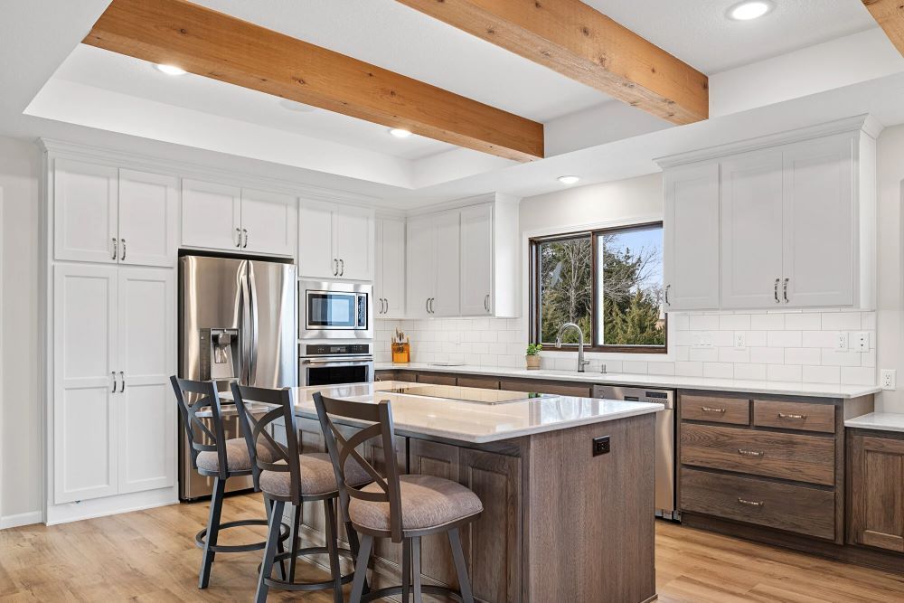 A kitchen with white cabinets, stainless steel appliances, a large island, and wooden beams.