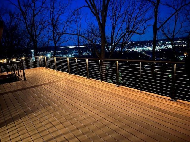 A wooden deck with a metal railing and a view of a city at night.