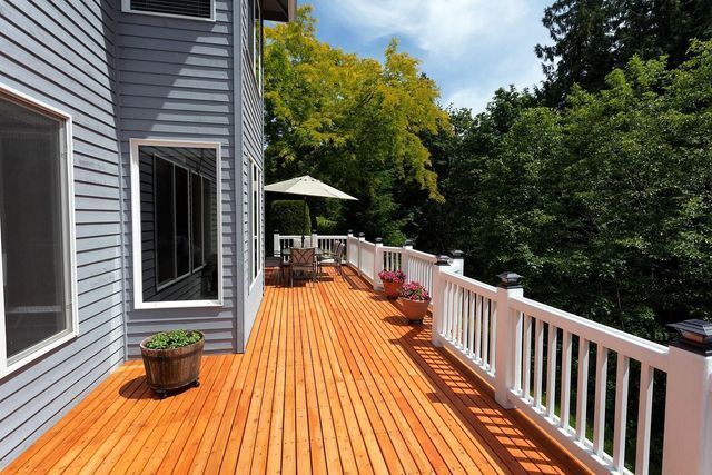 A large wooden deck with a white railing in front of a house.