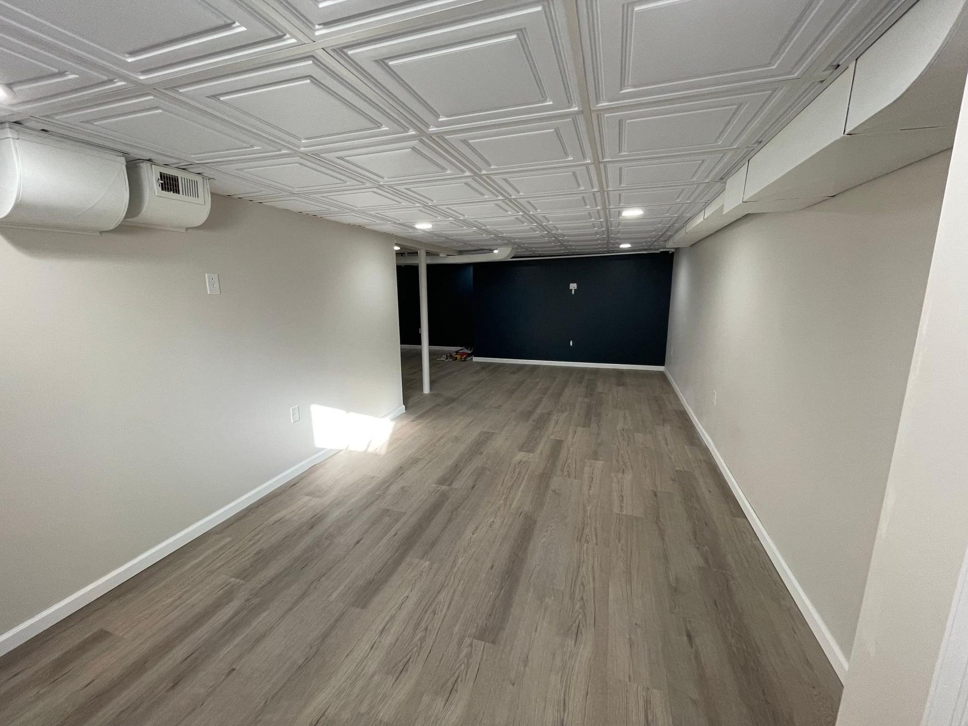 An empty basement with hardwood floors and a tiled ceiling.