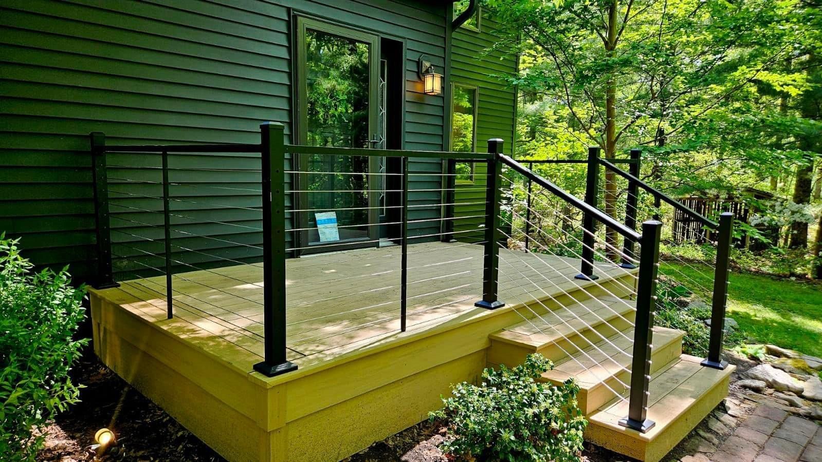 A yellow deck with a black railing and stairs next to a green house.