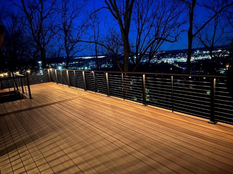 A wooden deck with a metal railing and a view of a city at night.