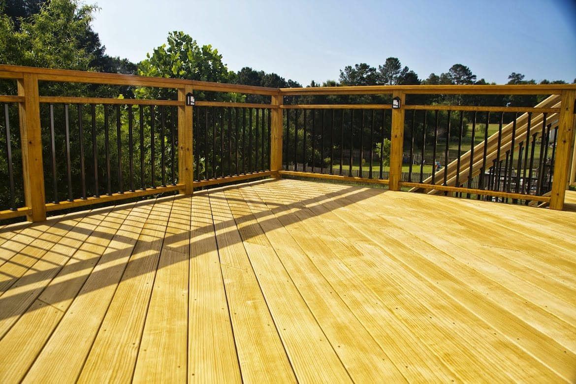 A wooden deck with a metal railing and trees in the background.