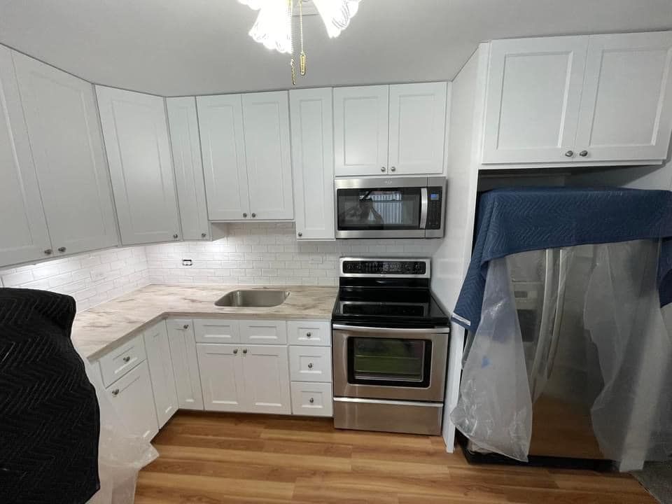A kitchen with white cabinets, a stove, a microwave, and a refrigerator.
