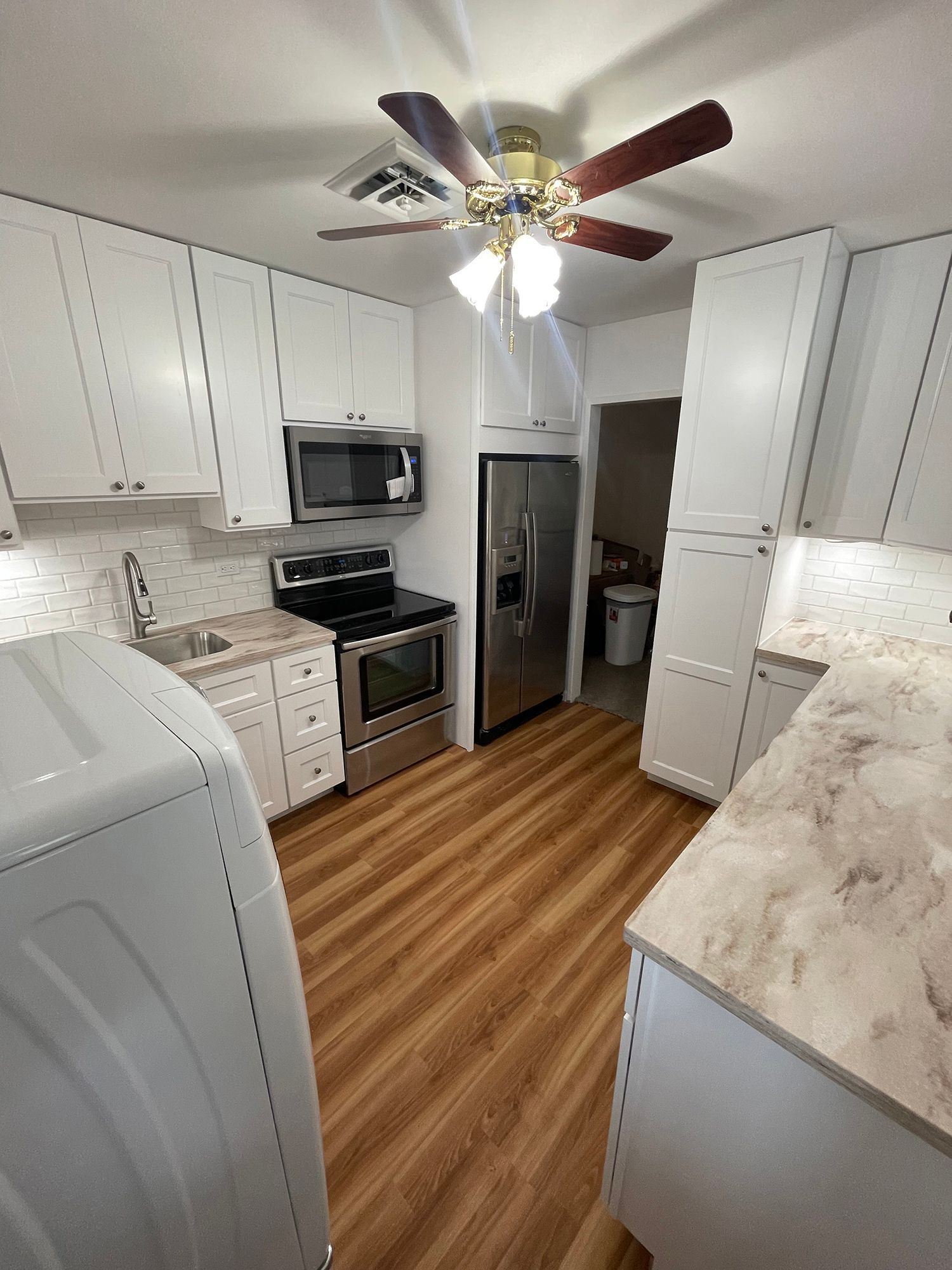 A kitchen with white cabinets, stainless steel appliances, a ceiling fan, and a washer and dryer.