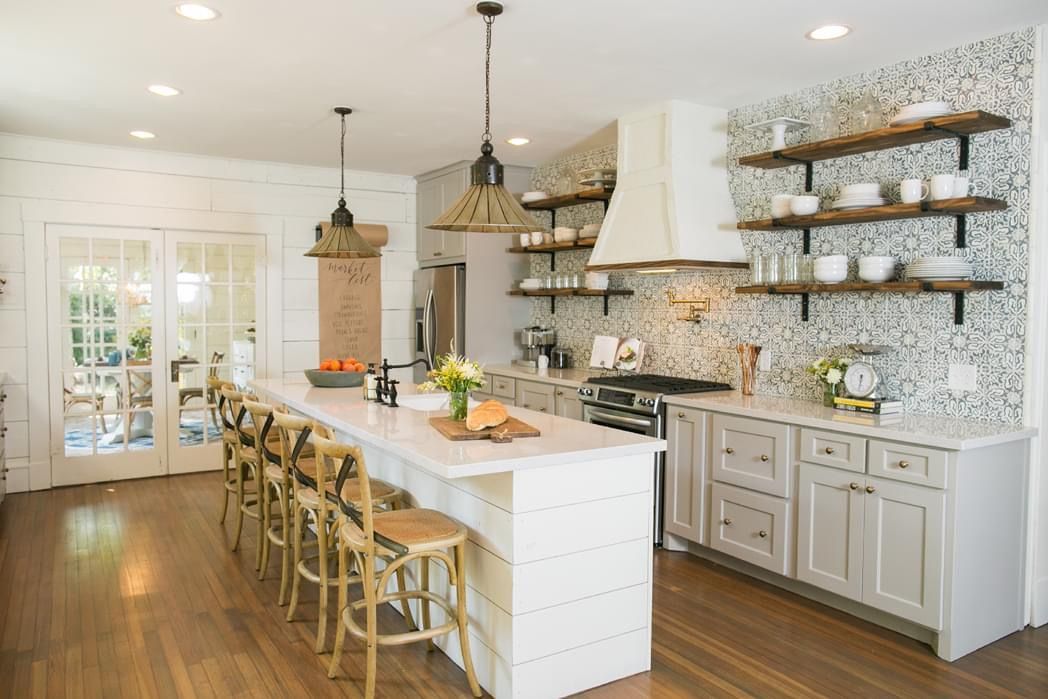 A kitchen with white cabinets, stools, a stove, and a large island.