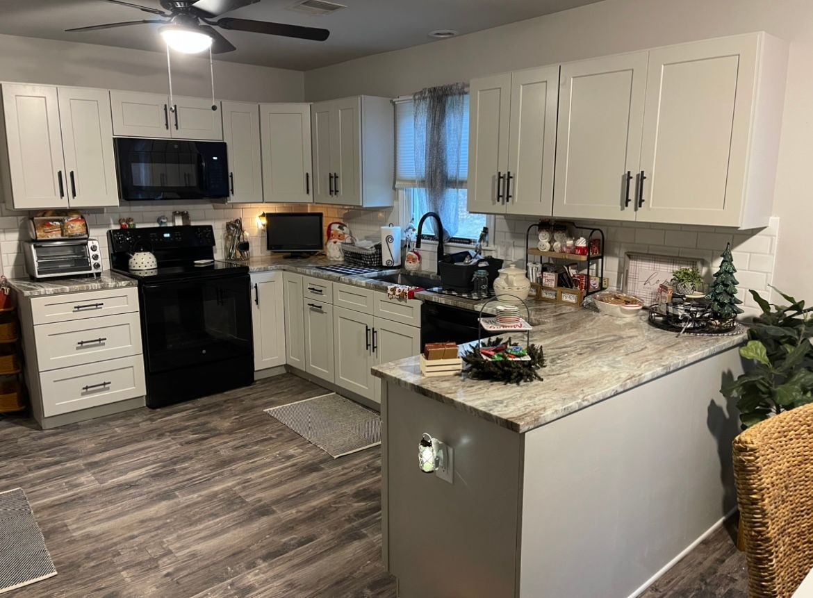 A kitchen with white cabinets, a black stove, a microwave, and a ceiling fan.