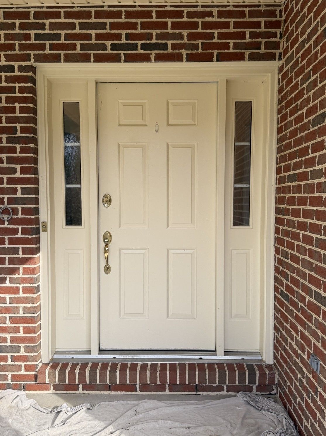 Cream-colored front door with sidelights, set in a brick frame. Doorknob and handle visible.