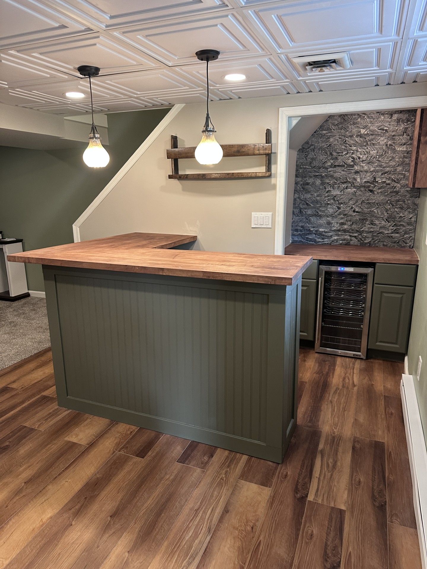 Basement bar with wooden countertop, olive green cabinet, wine fridge, and pendant lights.