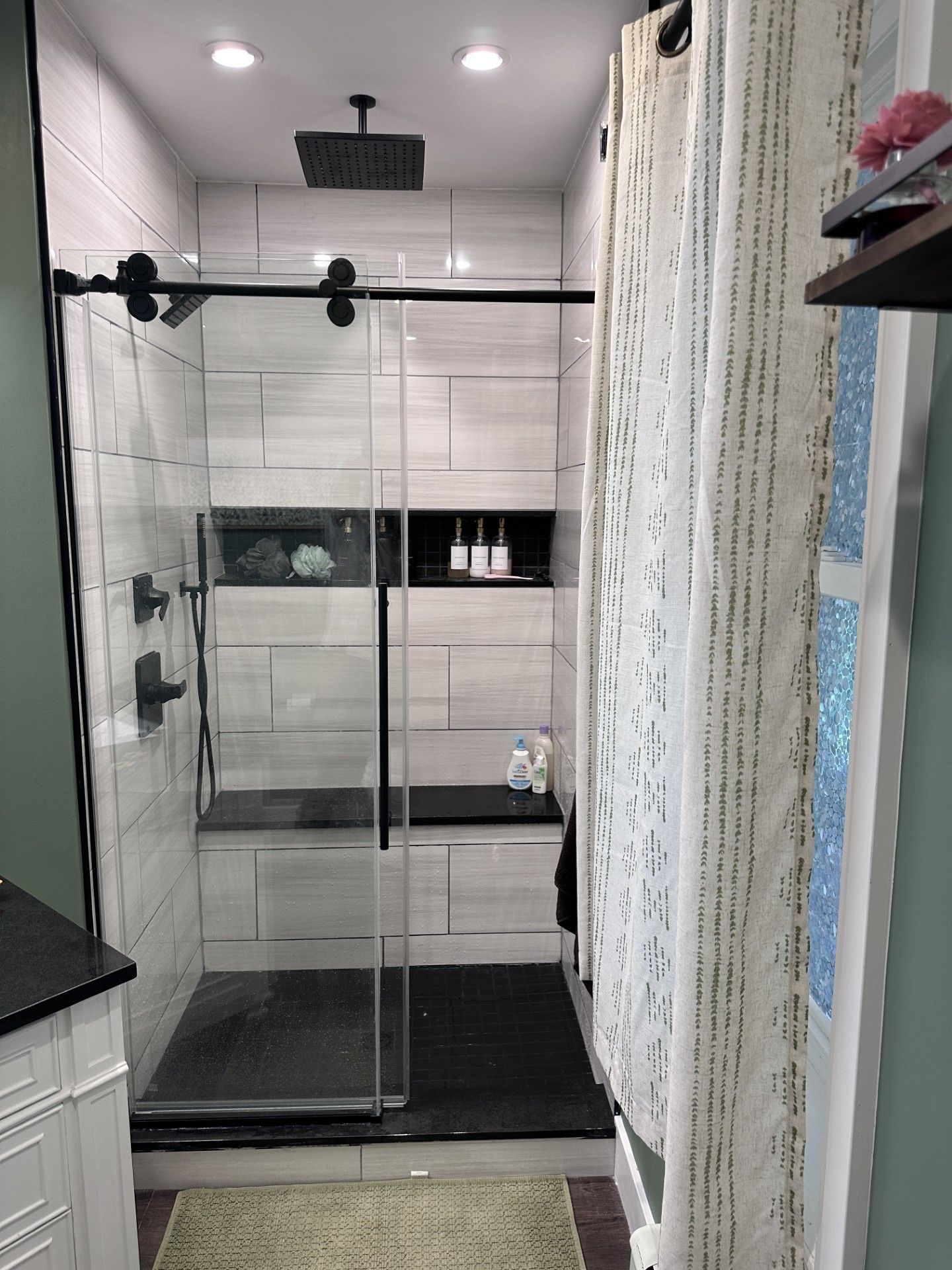 Modern bathroom with glass shower, black fixtures, and light-colored tile walls.
