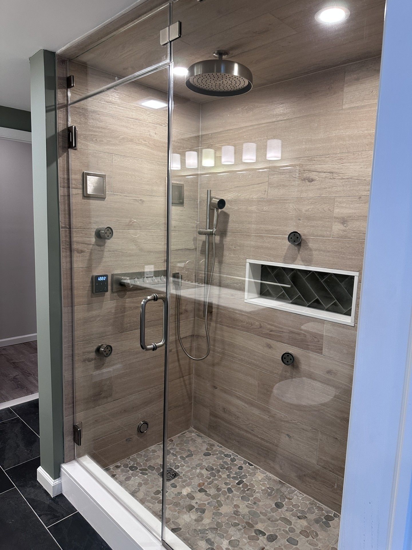 Modern, glass-enclosed shower with stone tile walls and pebble floor. Includes rain showerhead, body jets, and recessed shelf.