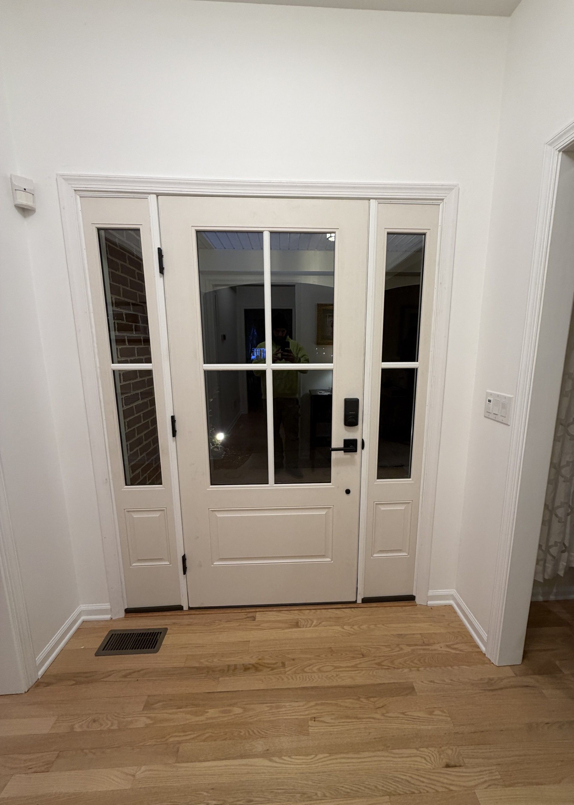 White front door with sidelights, wooden floors, and a brick wall visible on the left.