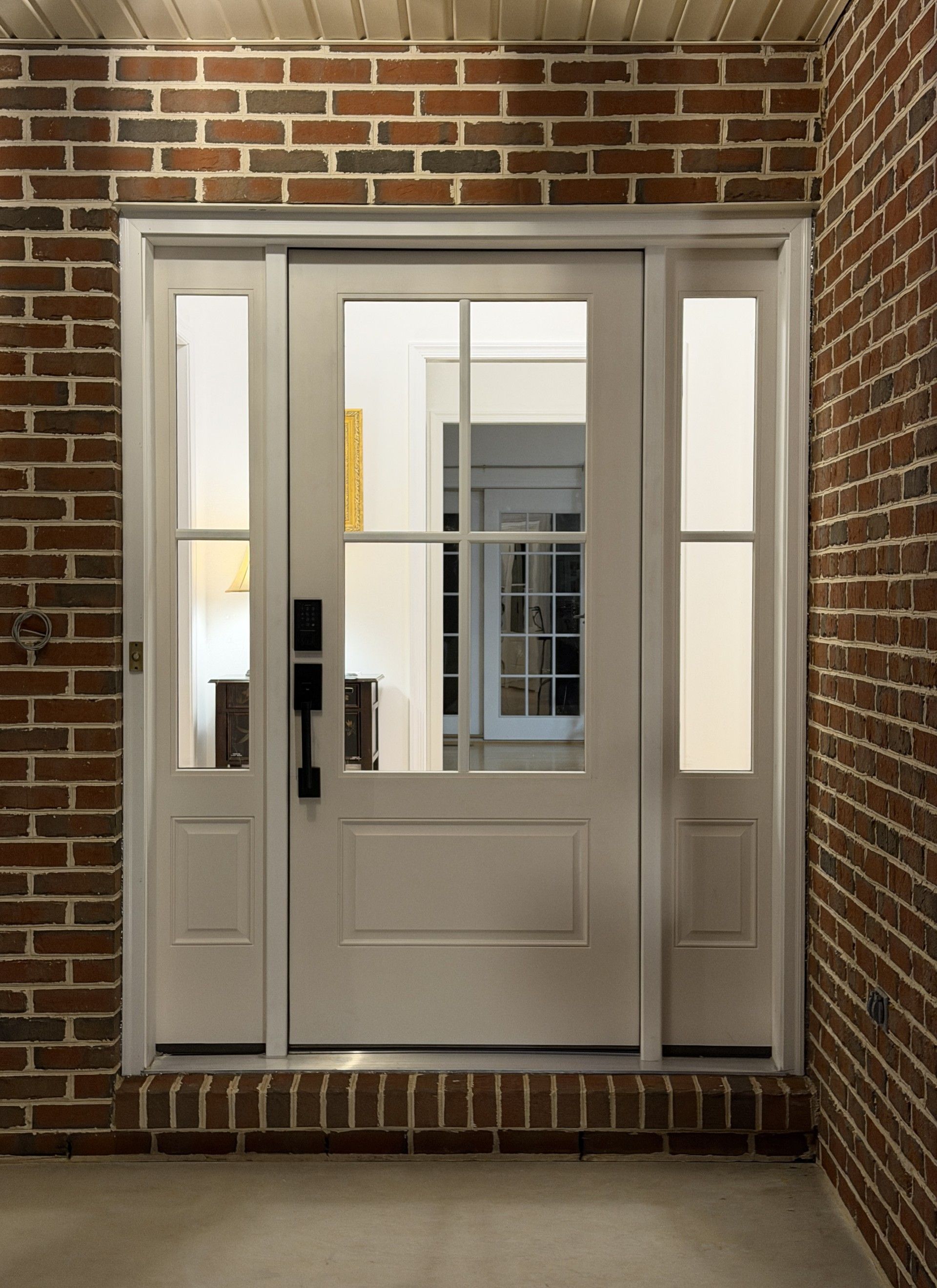 White front door with sidelights, set in a brick wall. The door has a glass pane and a black handle.