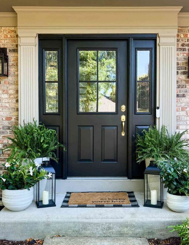 A black front door with glass panels framed in white, decorated with lanterns and potted ferns on a concrete porch.