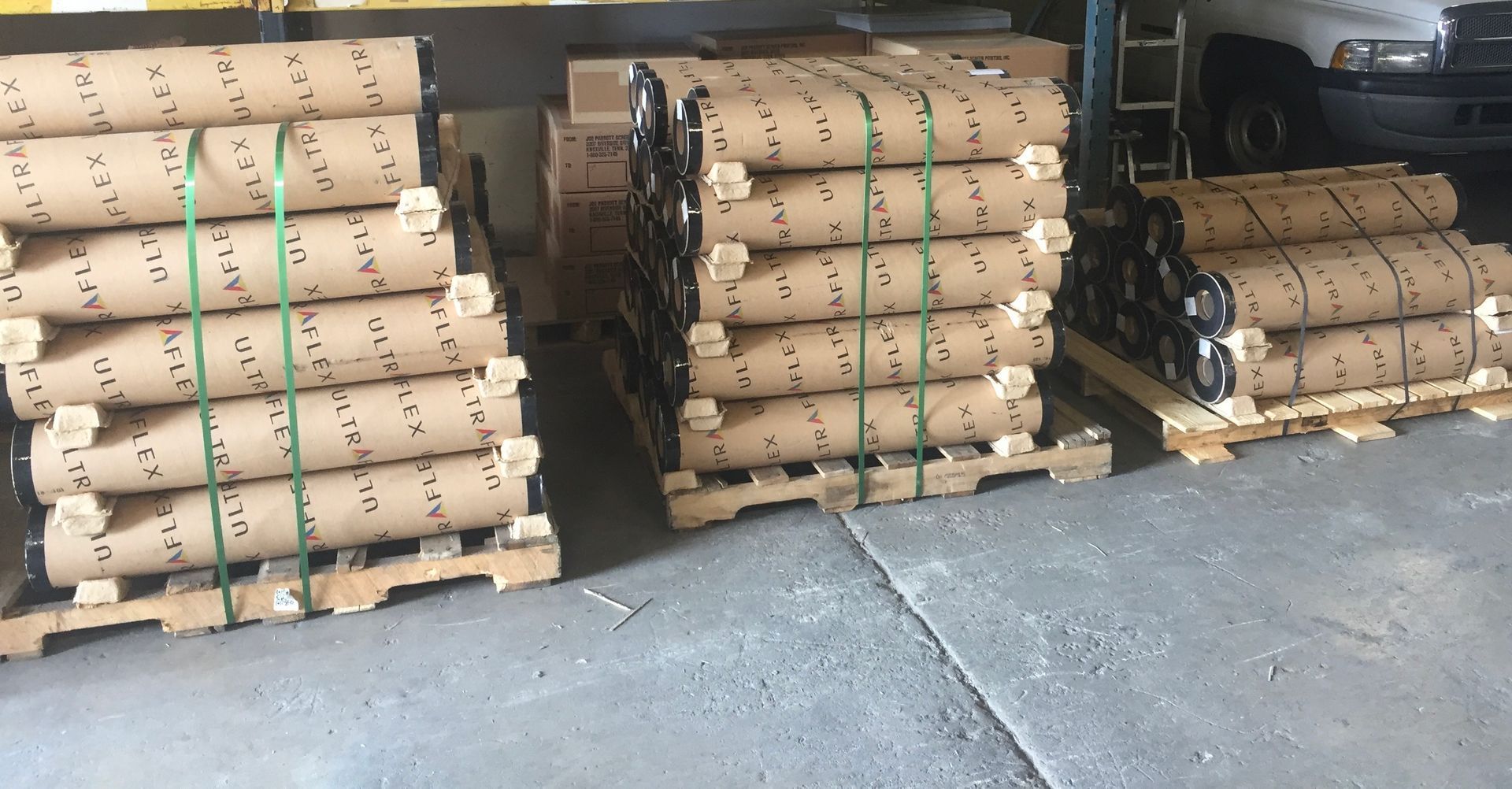 Pallets of rolled-up material secured with green straps, inside a warehouse.
