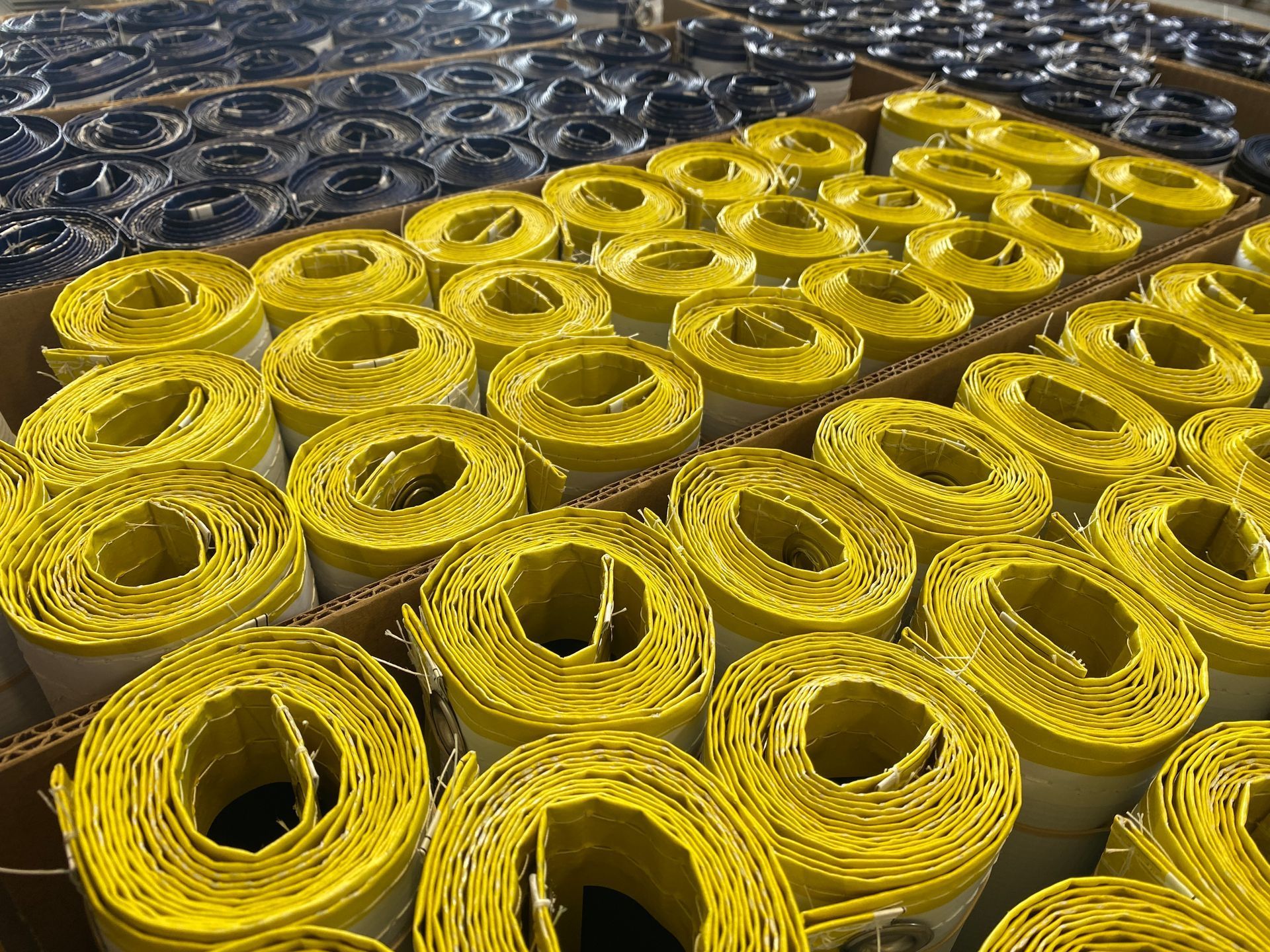 Yellow-wrapped rolls, likely construction material, stacked in a cardboard box, with similar black rolls in the background.