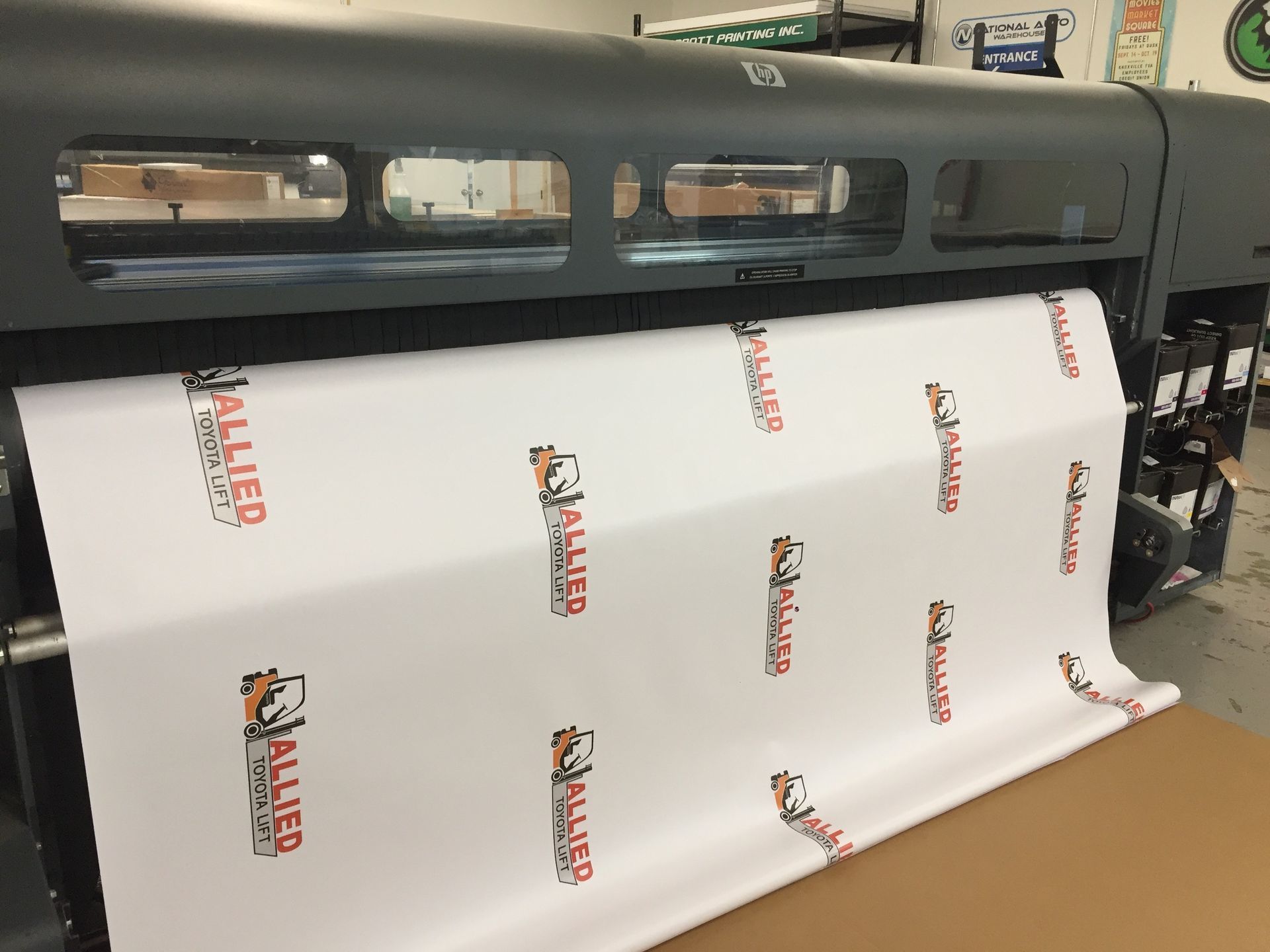 Large format printer printing a white banner with repeating company logo in red and black.