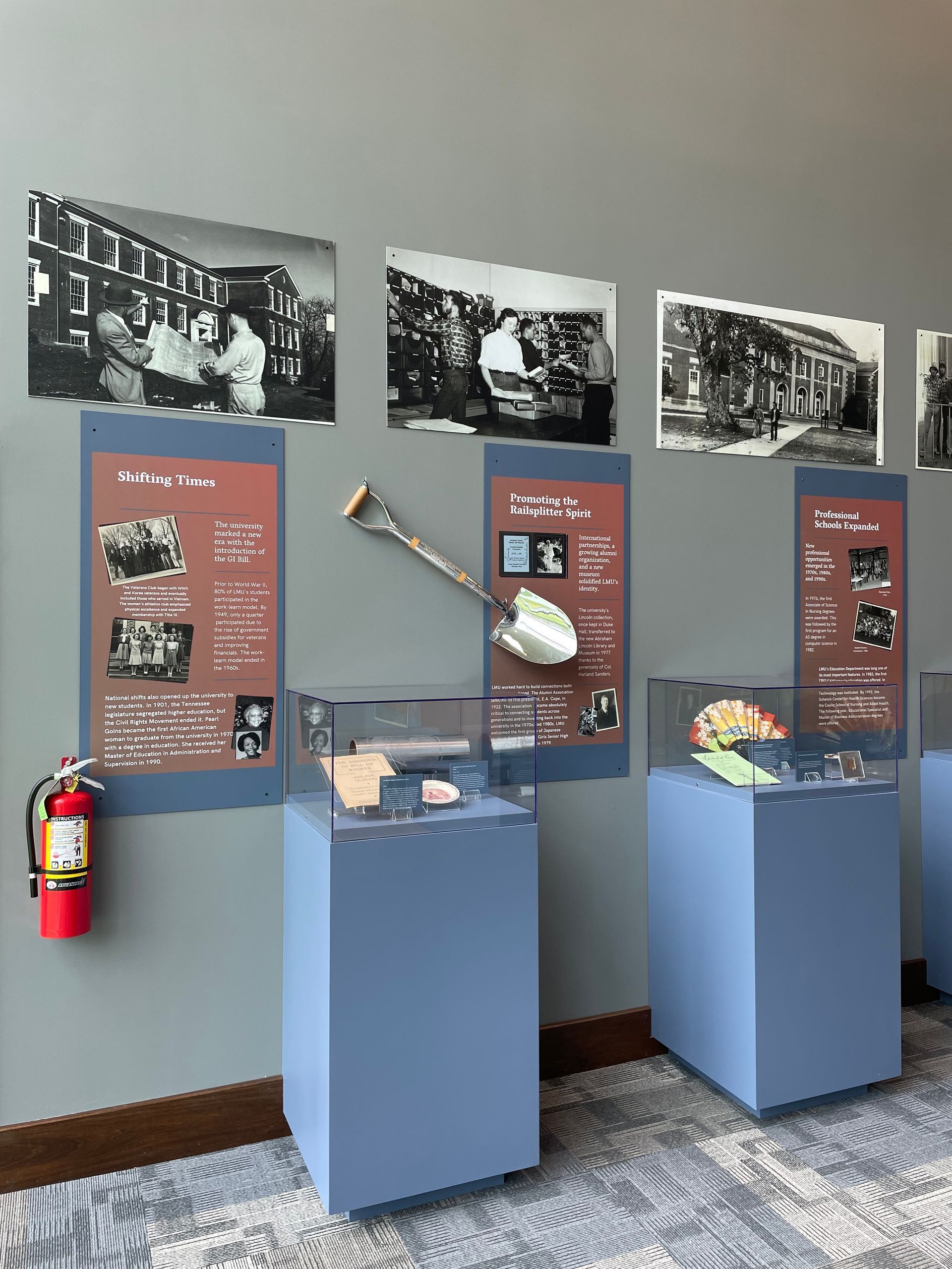 Museum exhibit: historical photos, display cases, a shovel, fire extinguisher, and informational panels.