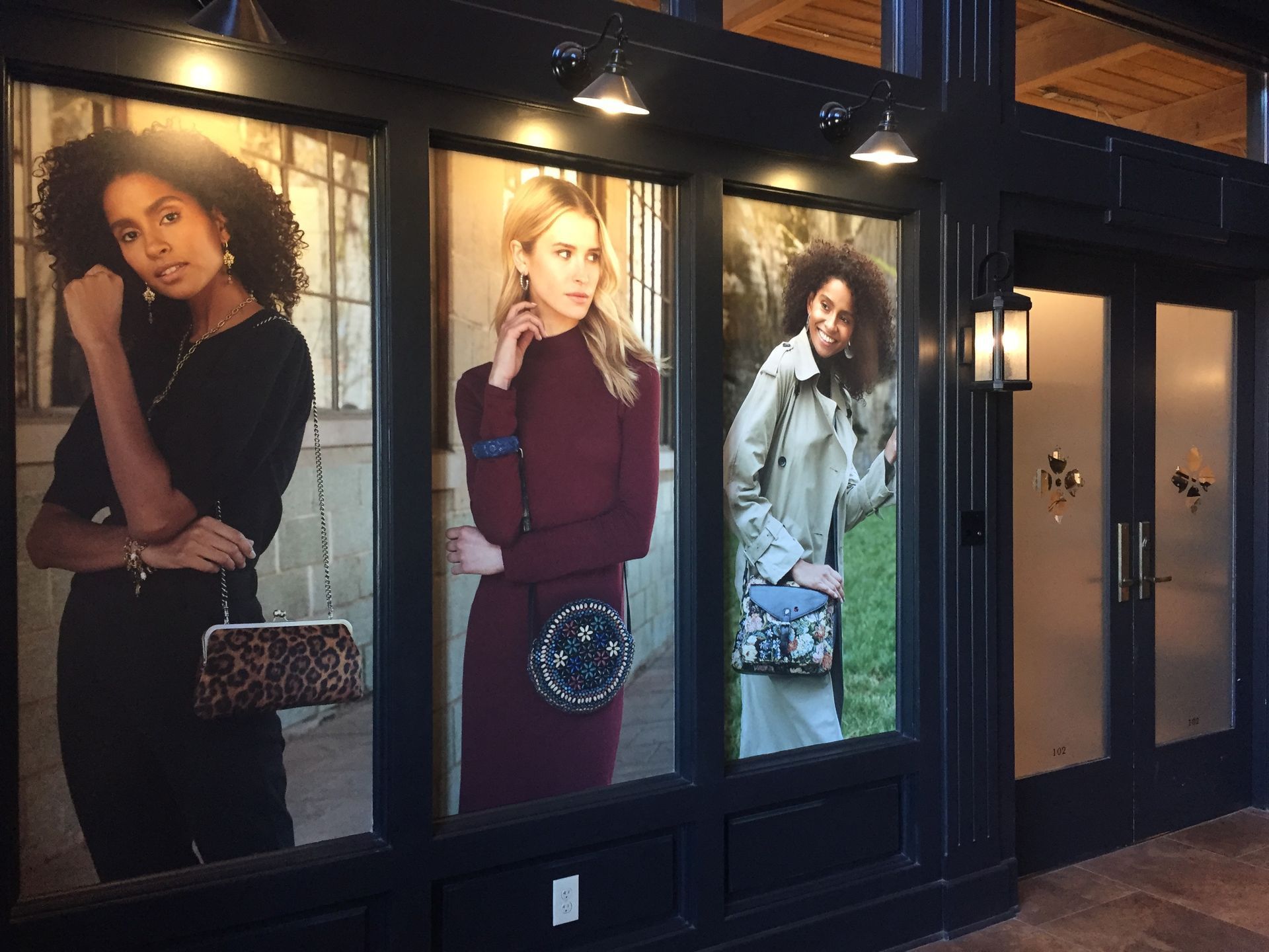 Storefront with three women in colorful outfits, holding purses, standing in windows.
