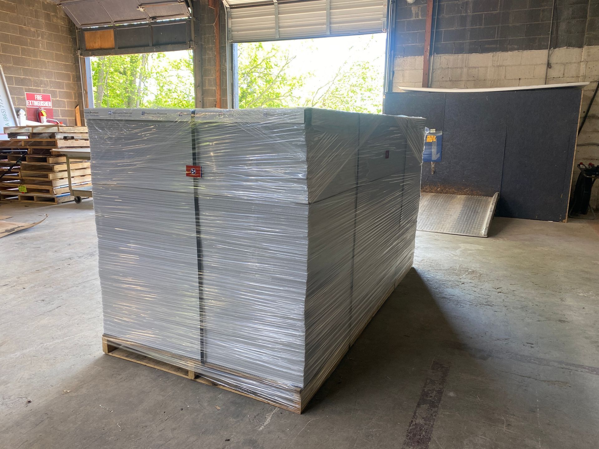 Pallet of wrapped silver metal sheets in a warehouse setting, next to a loading dock.