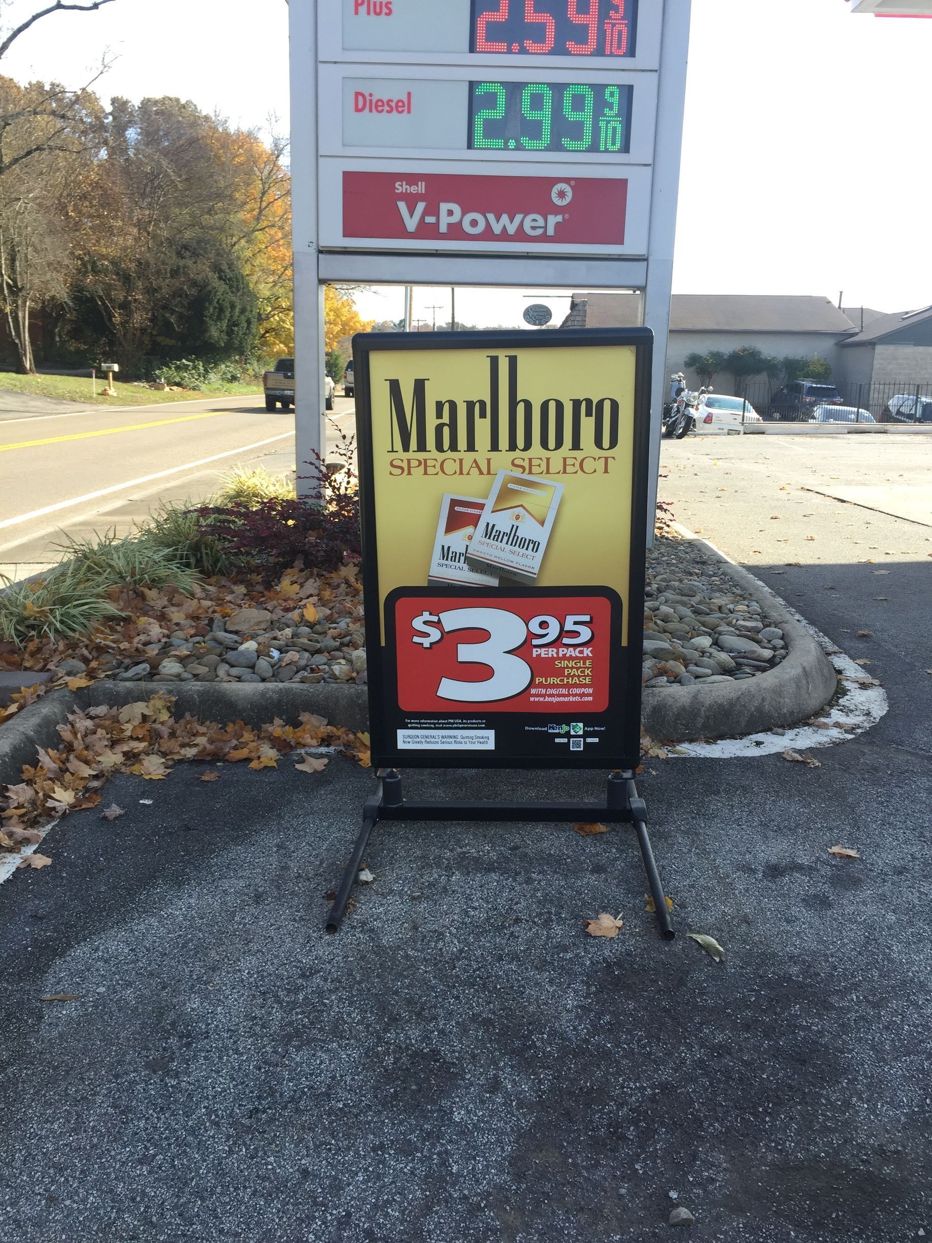 Sign advertising Marlboro Slim Select cigarettes for $3.95 near a gas station price display.