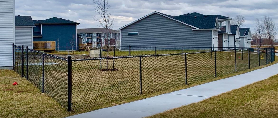 A chain link fence surrounds a yard in a residential neighborhood.