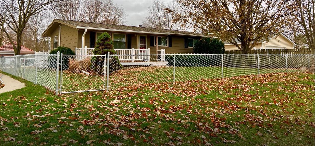 A house with a chain link fence around it and a lot of leaves on the ground.