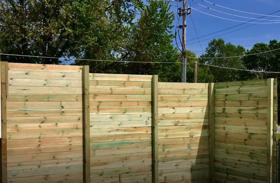 A wooden fence is surrounded by trees and power lines.