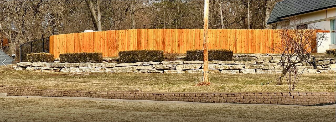 A wooden fence surrounds a stone wall in a yard.