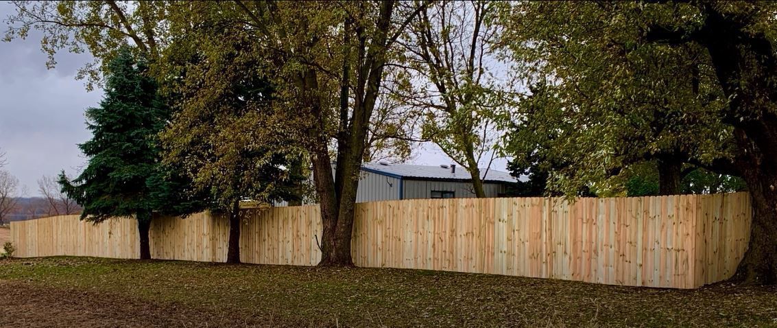A wooden fence is surrounded by trees in a field.