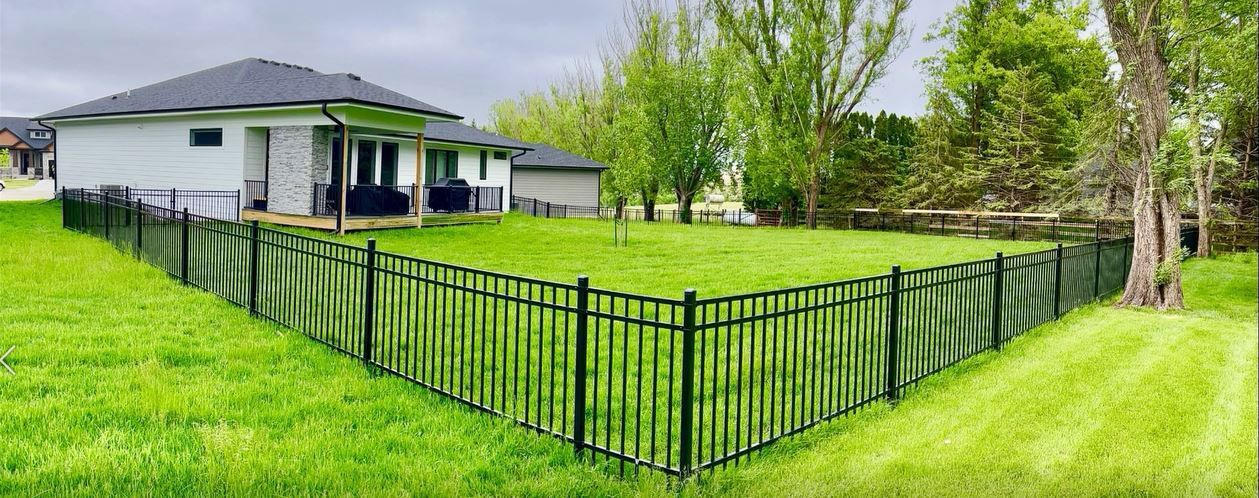 A black fence surrounds a lush green field in front of a house.